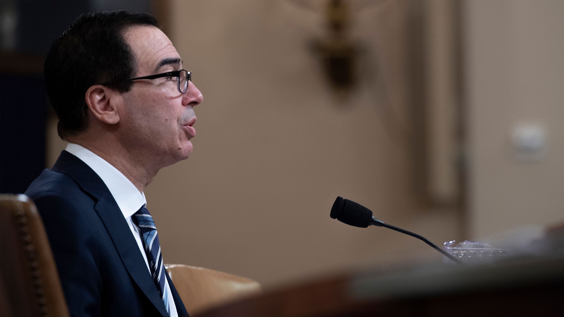 In this image, Mnuchin sits and talks into a microphone at a committee hearing.