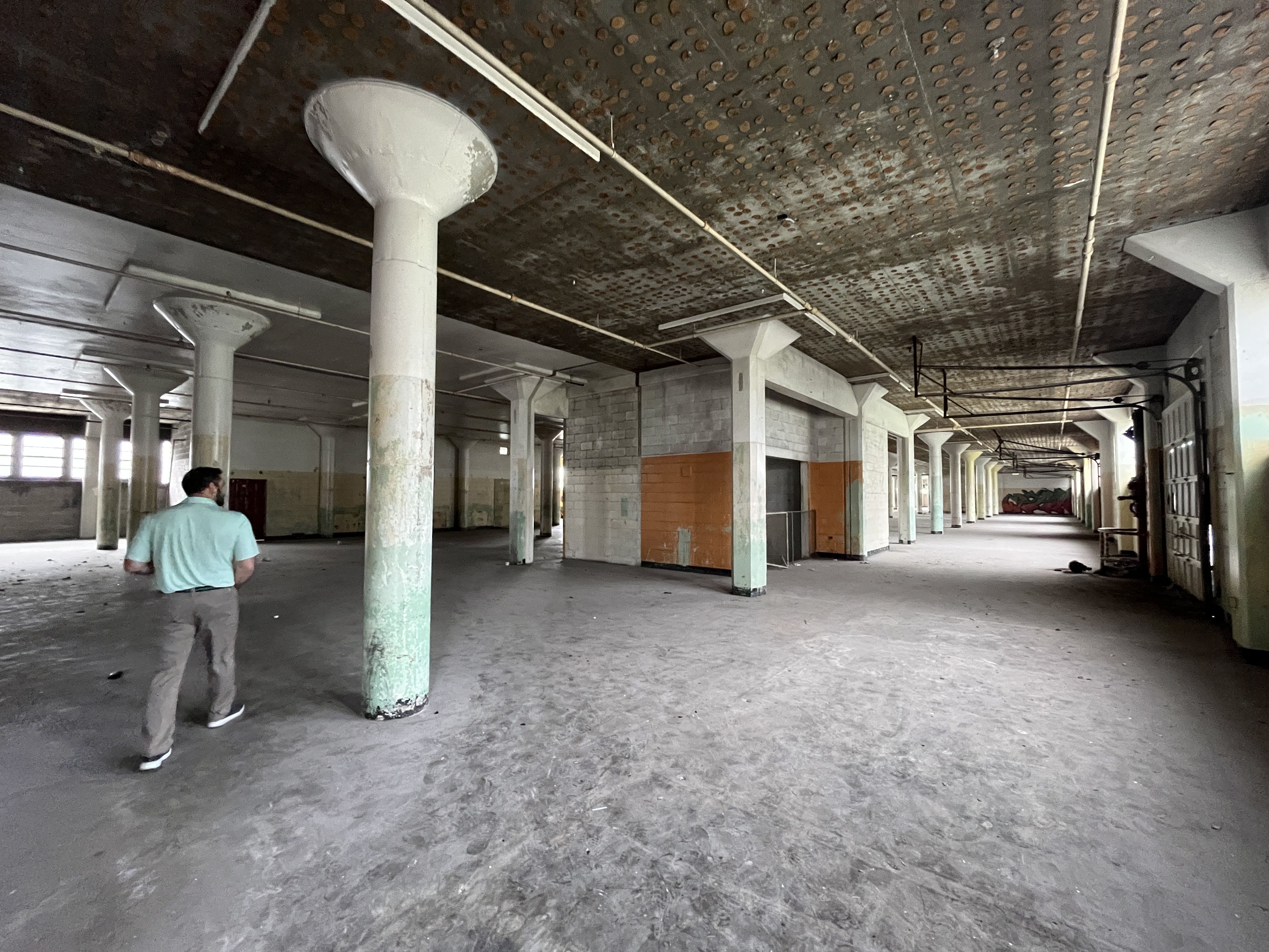 Photo shows the inside of a building that will be converted into a public market, empty other than rows of pillars and graffiti.