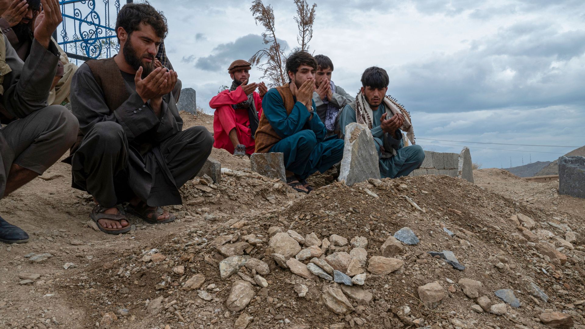 Afghans pray at a grave of victims, after burial ceremony in a cemetery on the outskirts of Kabul on August 18, 2022