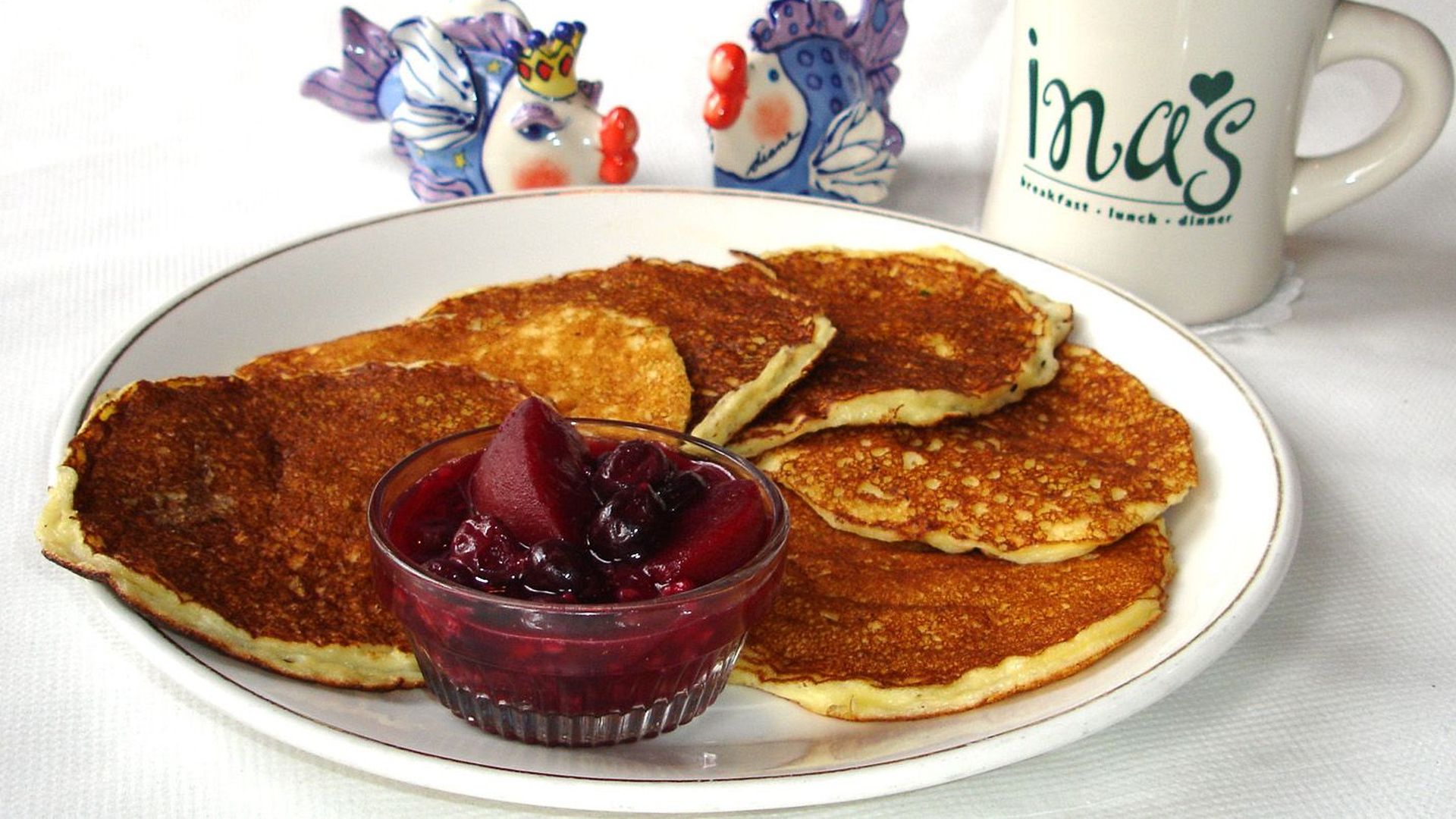 Ina's Heavenly Hots Pancakes served on a white plate with a coffee mug that says "Ina's."