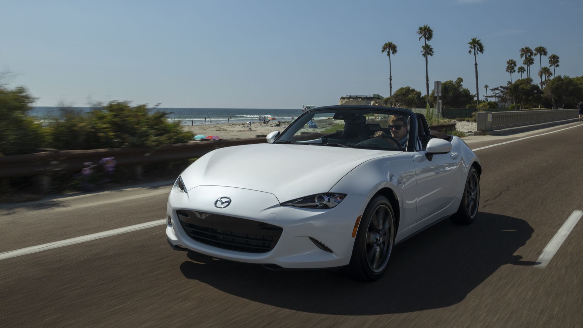 Image of a white Mazda Miata convertible driving along the coast