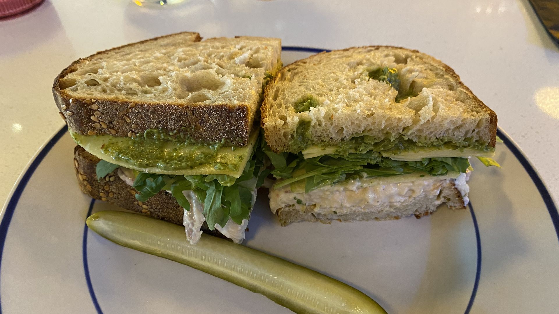 A sandwich that's been cut in half on a plate with a pickle spear.