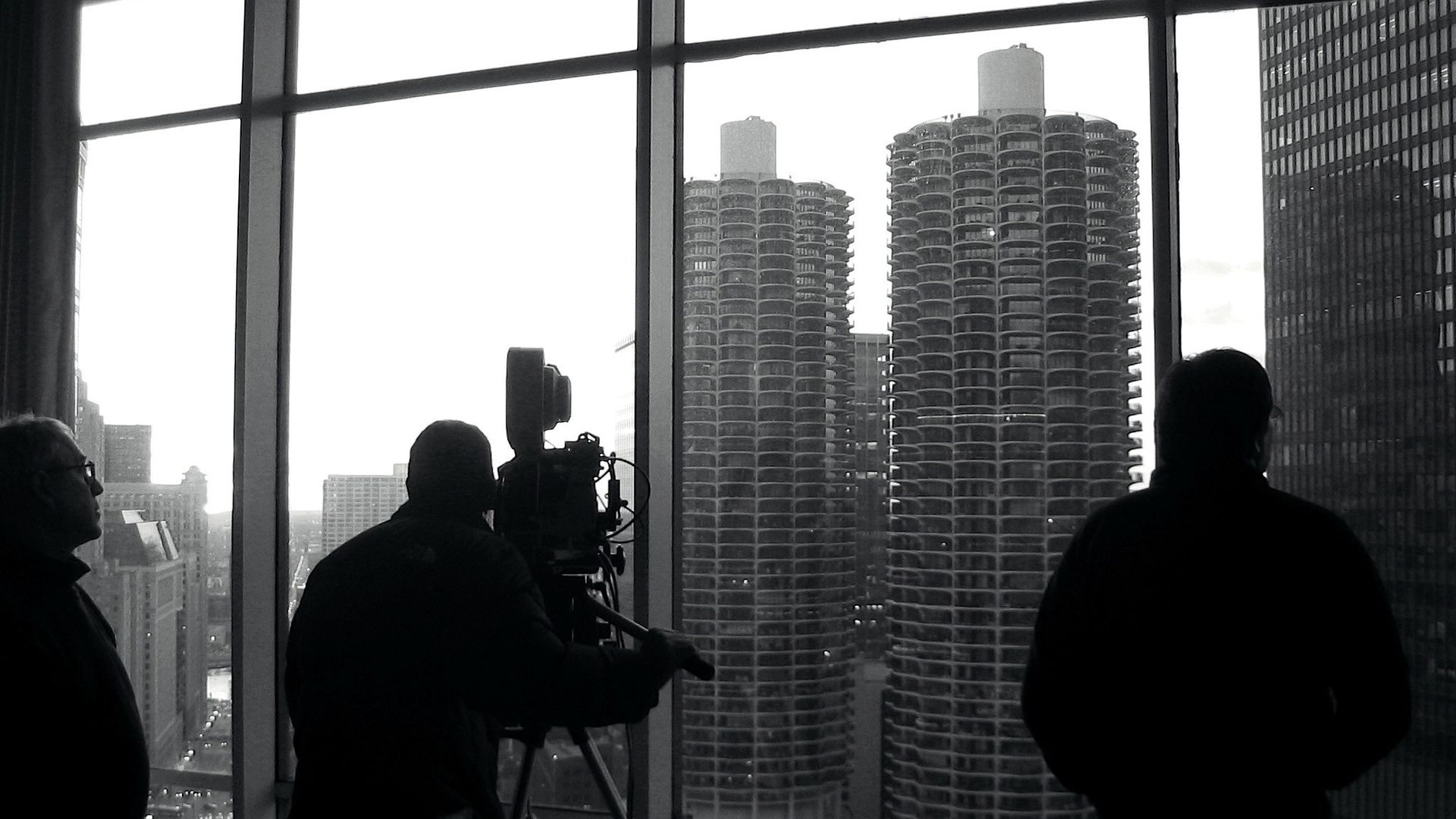 Black and white image of people looking out the window at Marina Towers, with one of them filming with a camera.