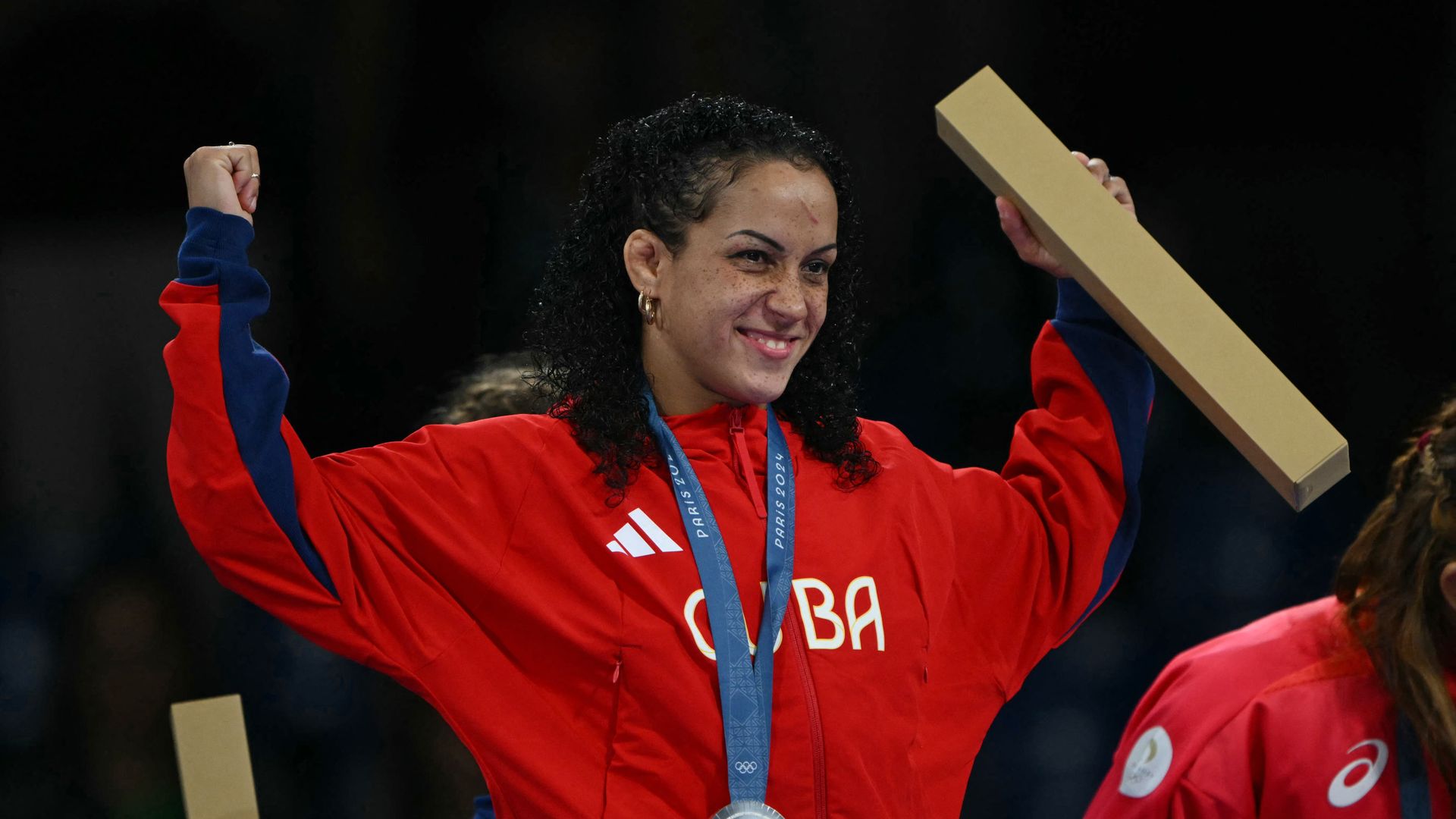 Cuban wrestler Yusneylys Guzmán holds both arms in the air while wearing her silver Olympic medal