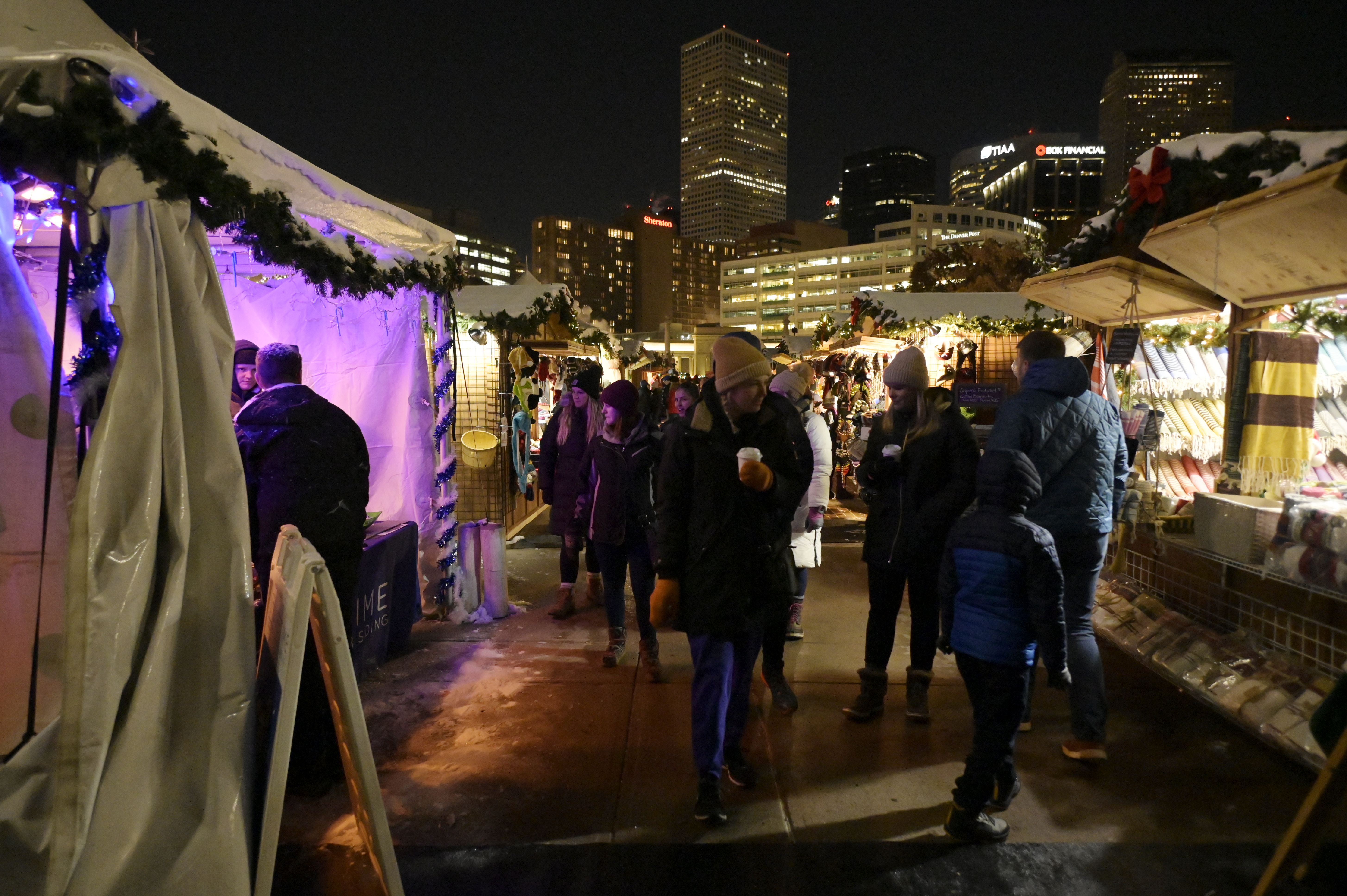 People in cold weather clothing walk through an outdoor market at night. 