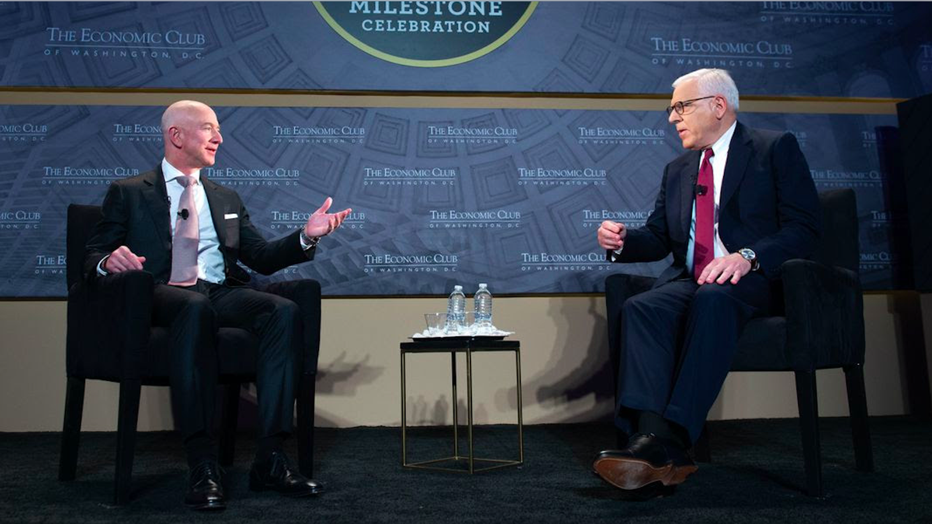 Bezos motions with his arms while talking to Rubenstein onstage