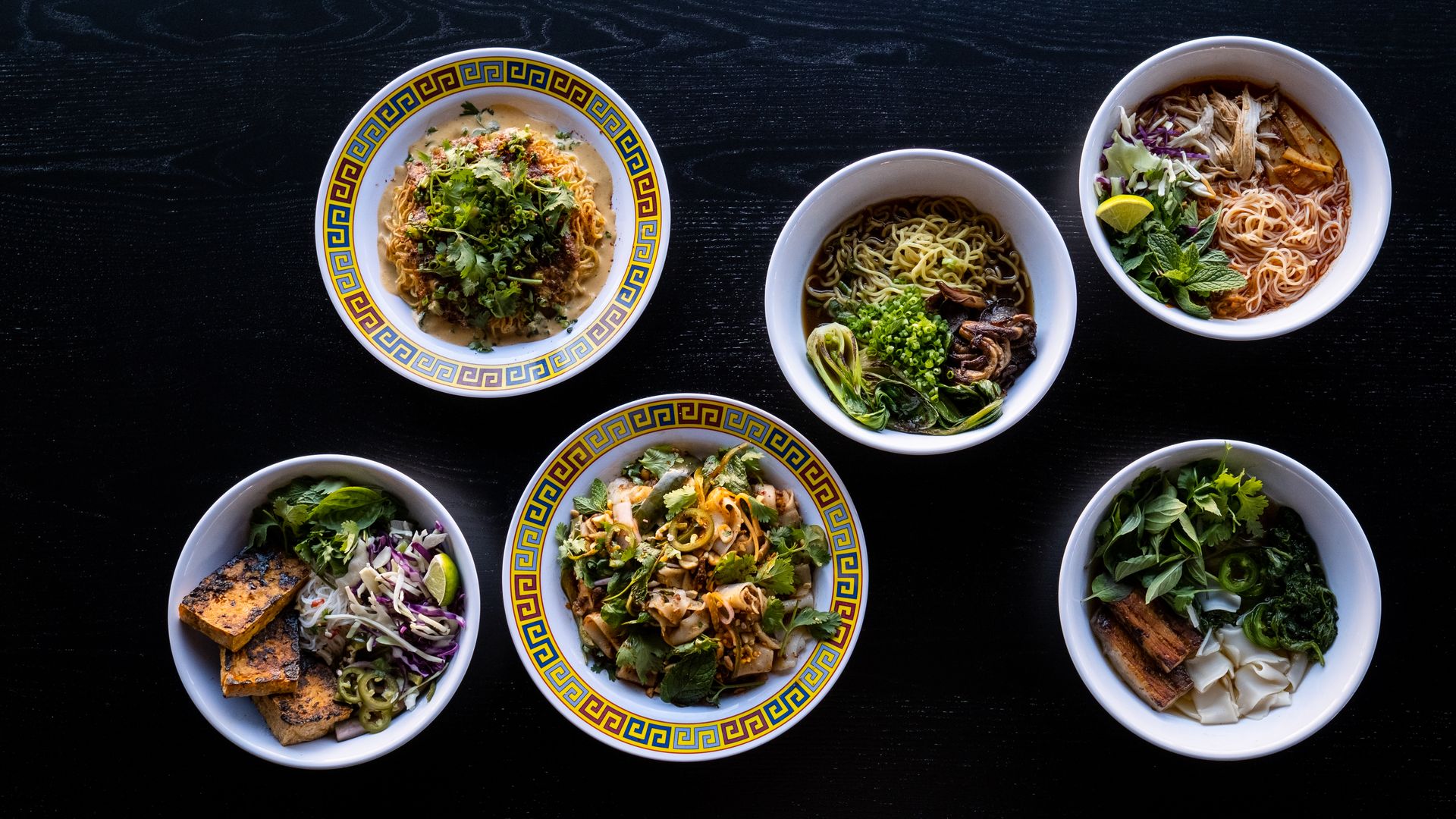 Six bowls of noodles arranged on a black background.