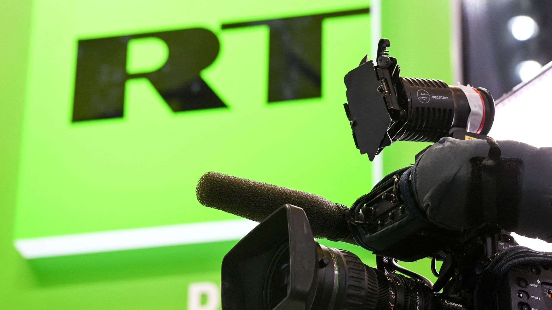 Photo of a video camera set up in front of a green wall with the RT logo on it