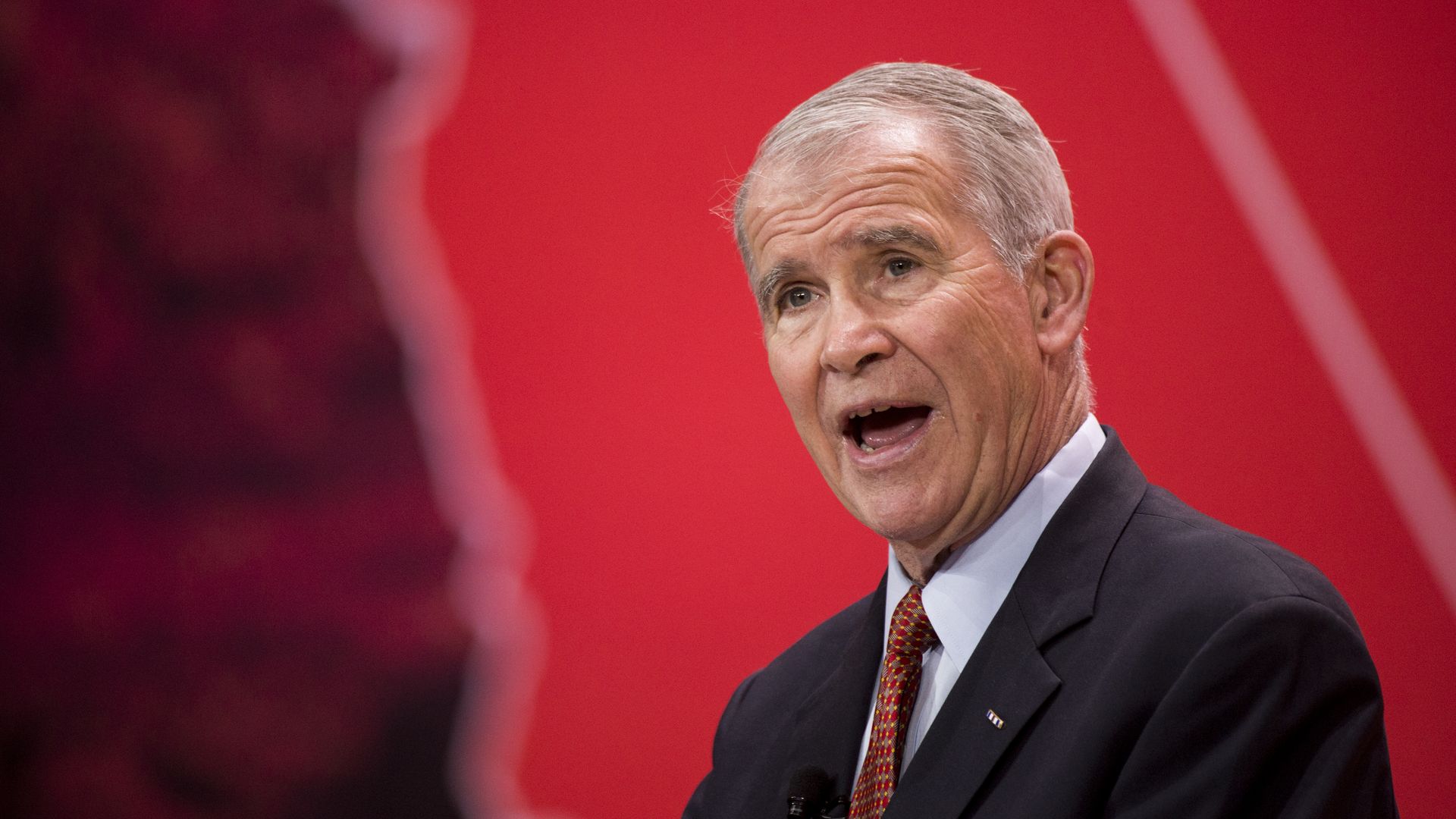 Oliver North speaking before a red background.
