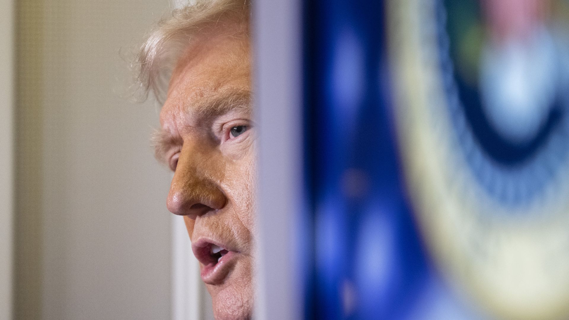 Donald Trump, partially obscured by a doorway, talks with reporters.