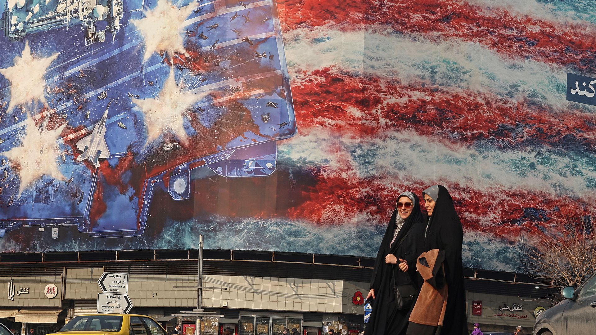 Women walking by a large anti-U.S. billboard at Enqelab Square in Tehran.