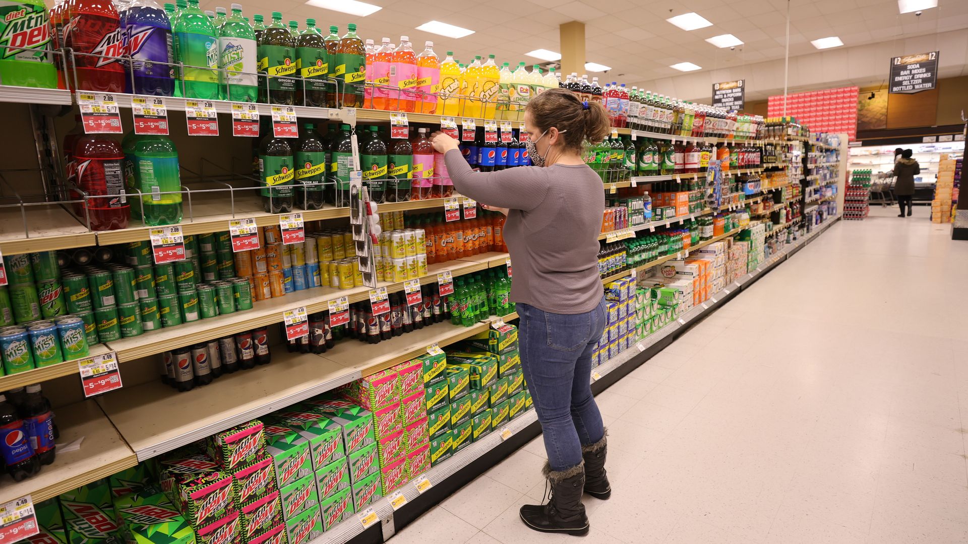 A shopper reaches for a drink in the soda aisle of a grocery store