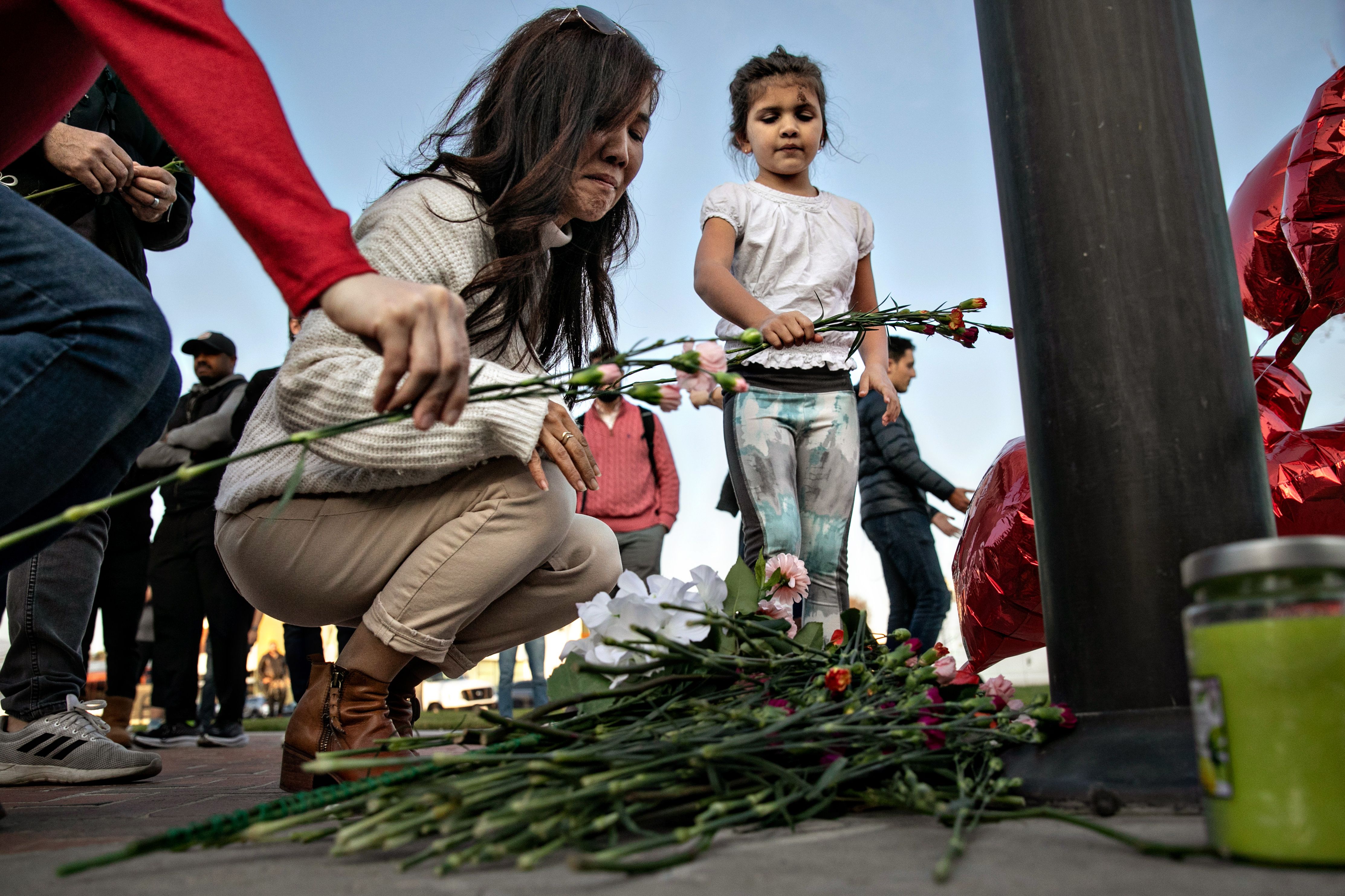 A woman and a little girl place flowers at a memorial where community members gathered for vigil to the ballroom dance studio mass victims on Sunday, Jan. 22, 2023 in Monterey Park, CA. 