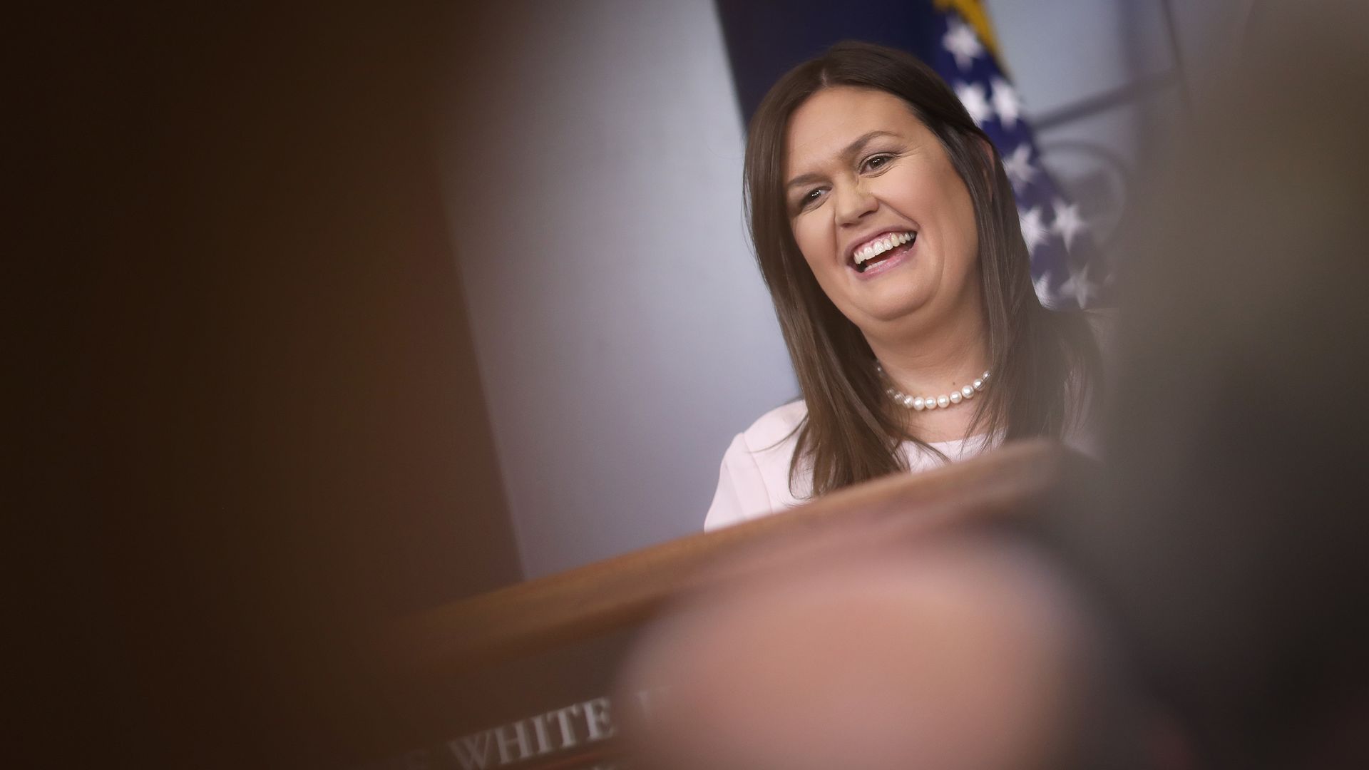 Sarah Sanders laughing from the podium through a blur of raised hands of reporters