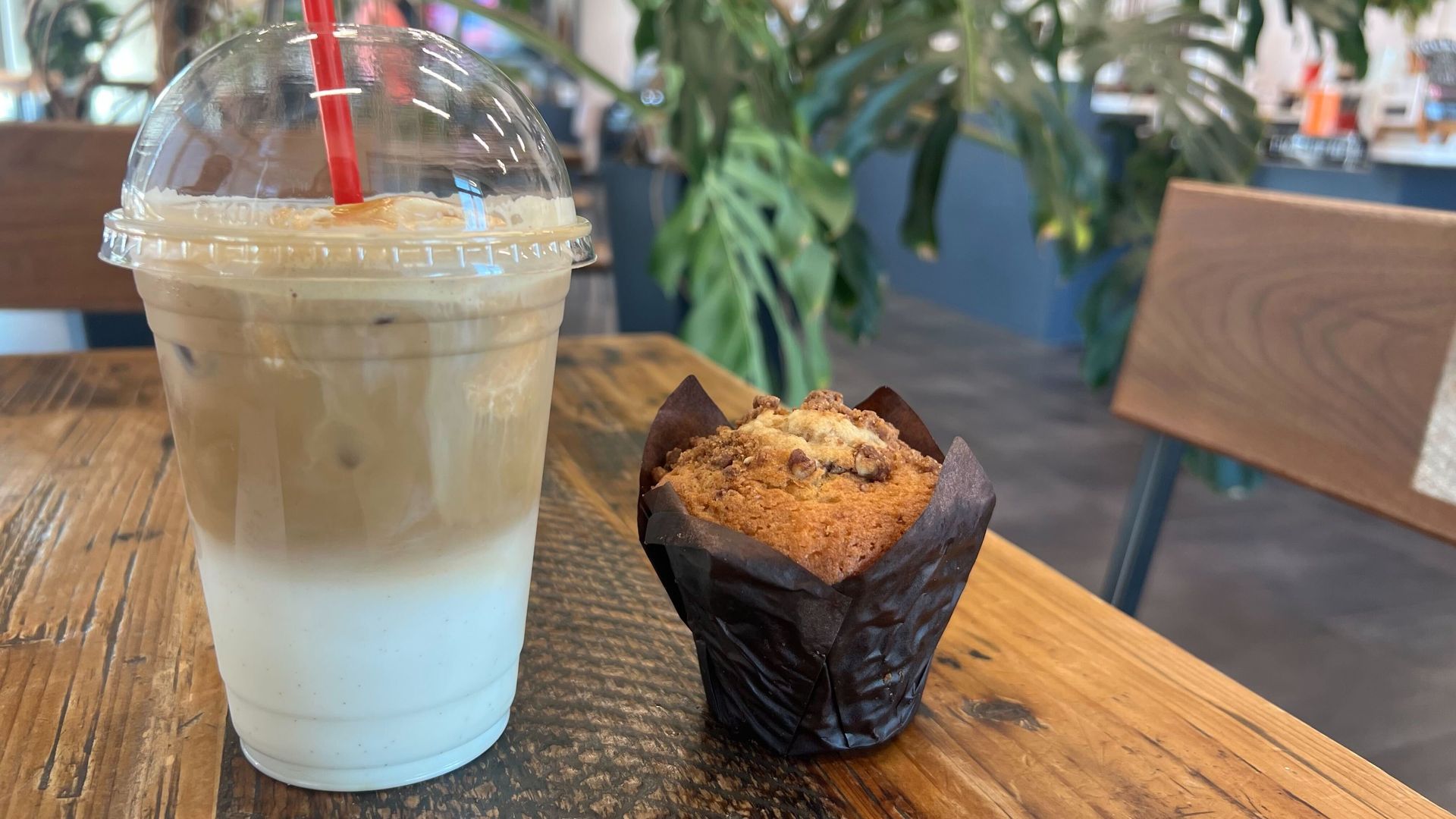 A photo of an iced latte with a muffin on a table inside a coffeeshop