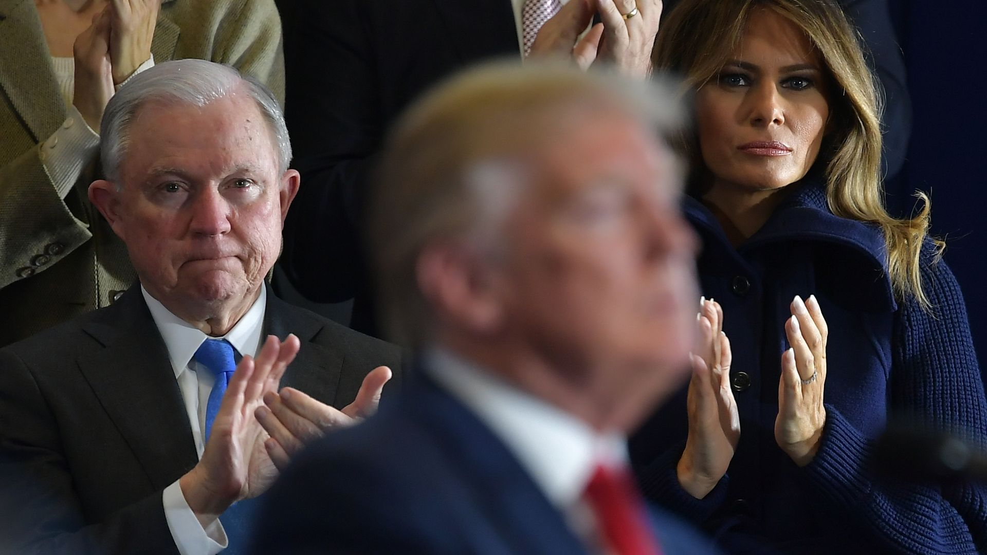 Jeff Sessions claps behind Donald Trump's blurry profile at a speech 