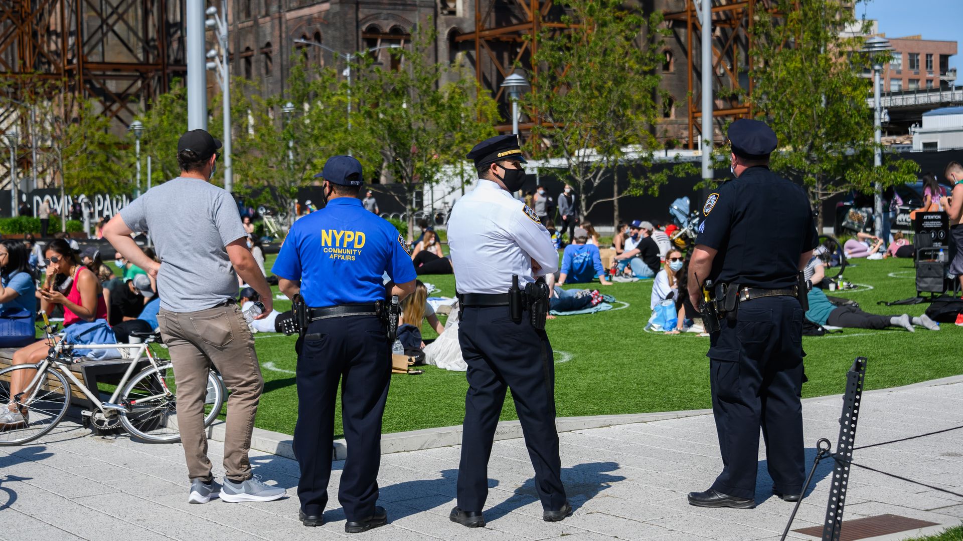 In this image, a line of NYPD police officers stand outside in a park