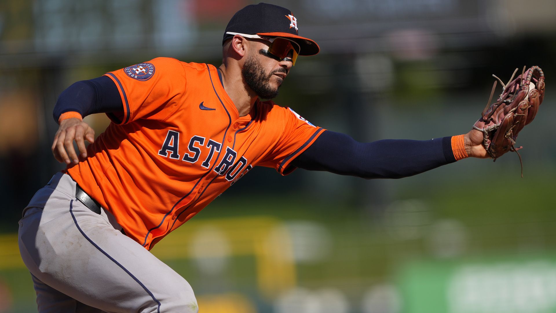 Astros' third baseman Carlos Correa, wearing an orange jersey and gray baseball pants, snags a baseball in his glove