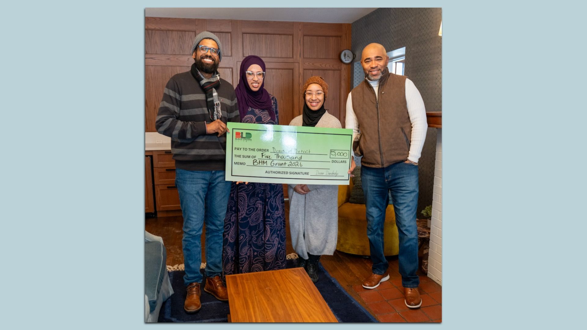 Four people smiling indoors, holding a large green check for $5,000 made out to Dream Detroit for BHM Grant 2026.
