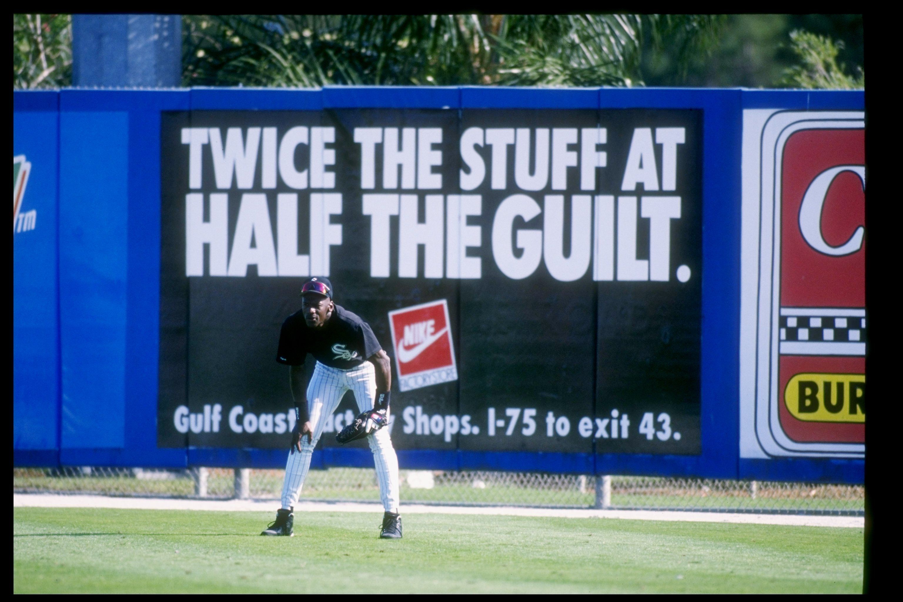 Photo of a man standing in outfield in front of a billboard for Nike. 