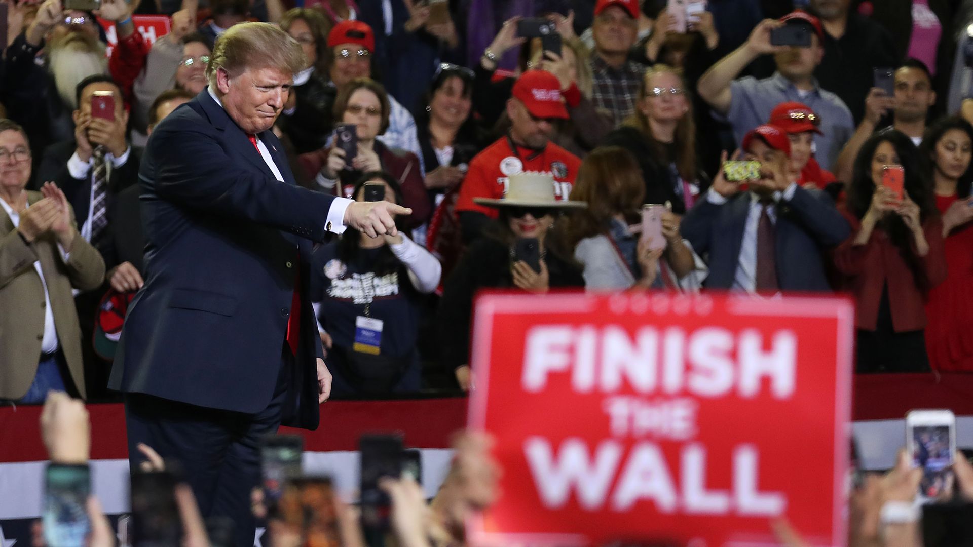 President Trump at a rally as a supporter holds a sign reading "Finish the Wall"