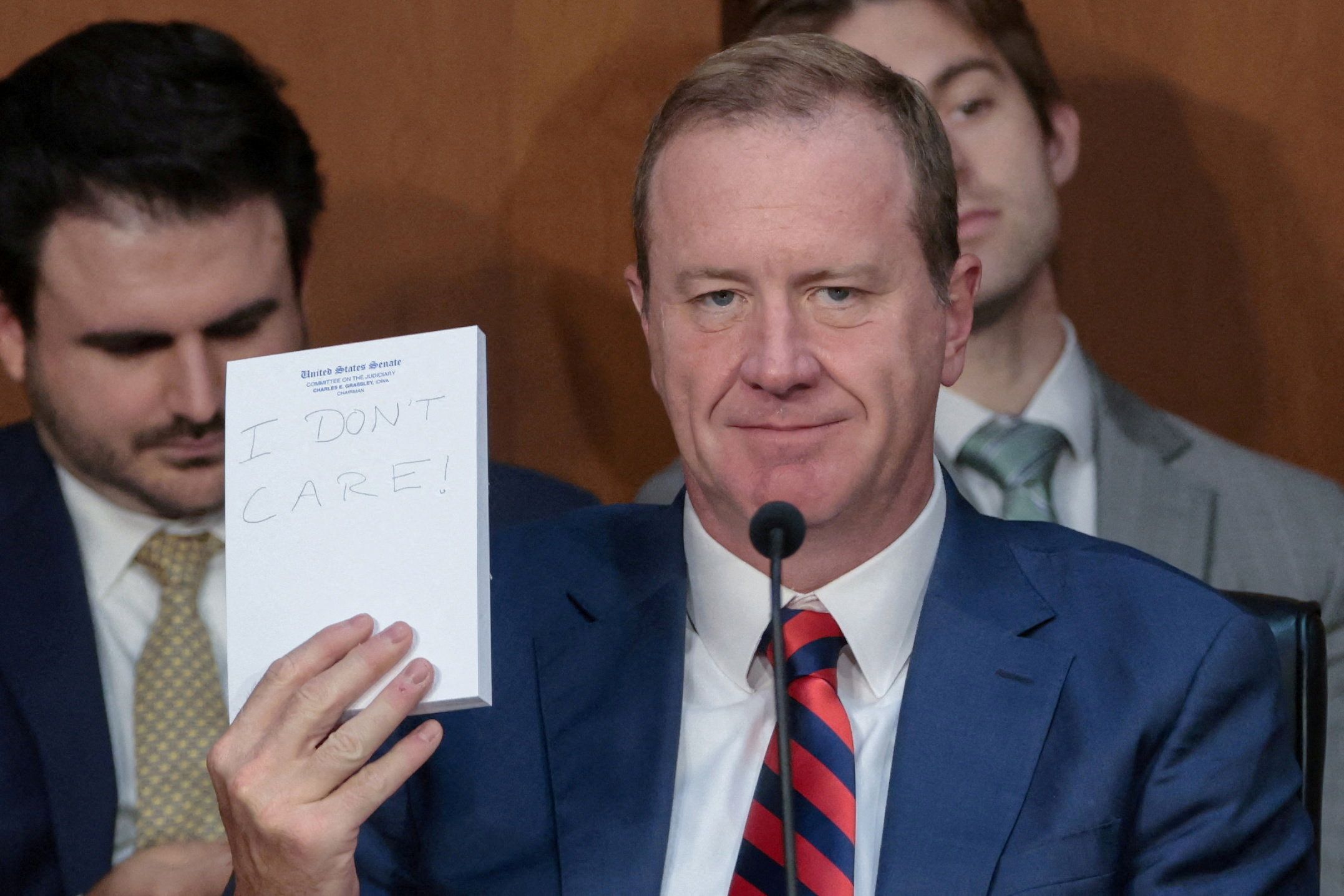 Sen. Eric Schmitt (R-Mo.) holds up a handwritten note — "I DON'T CARE!" — during remarks by Sen. Cory Booker (D-N.J.) during a confirmation hearing for Attorney General Todd Blanche earlier this month.