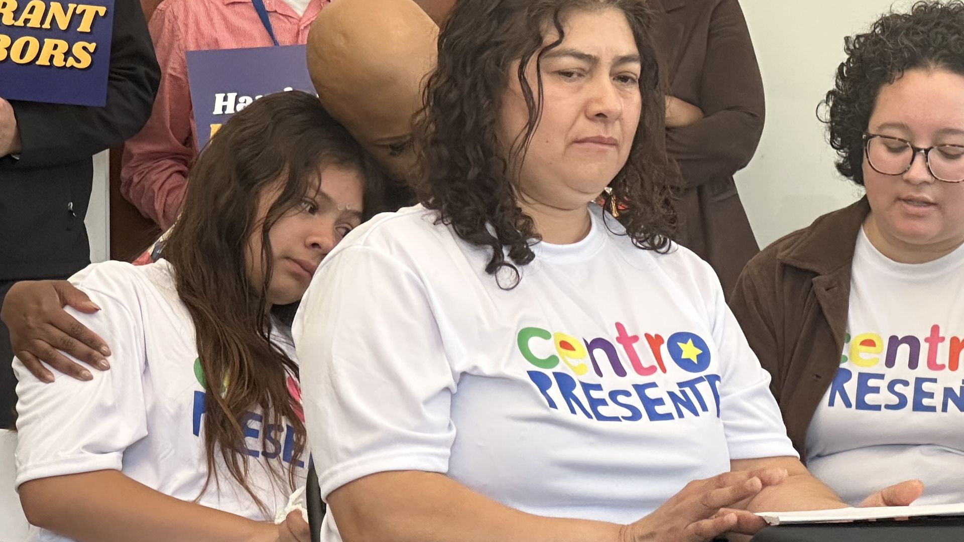 Mercedes Pineda, center, shares how her husband's ICE arrest affected her family and sits at a table. Seated behind her is U.S. Rep. Ayanne Pressley, who is hugging and comforting Pineda's 12-year-old daughter.