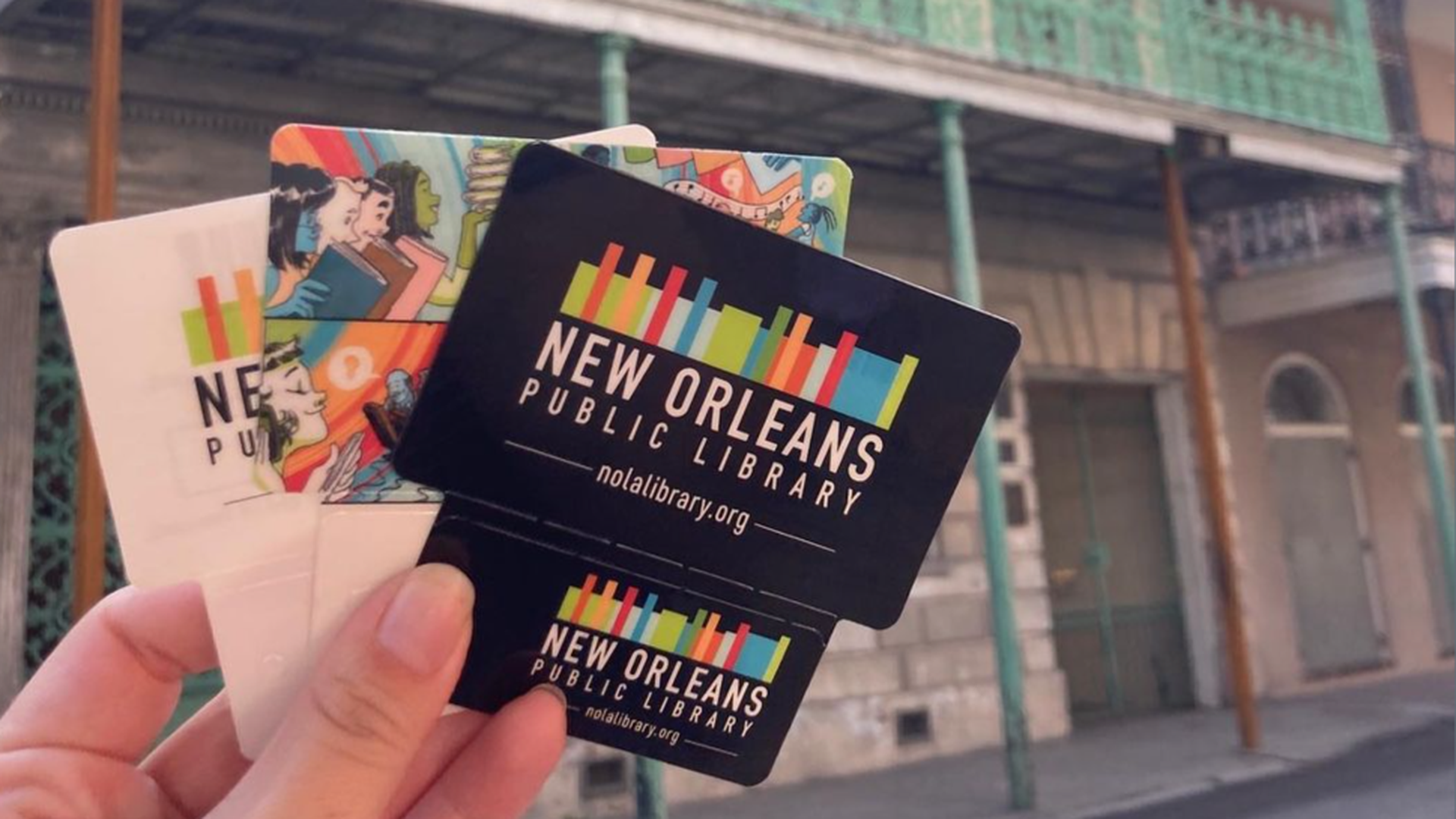 Photo shows a hand holding up three New Orleans library cards