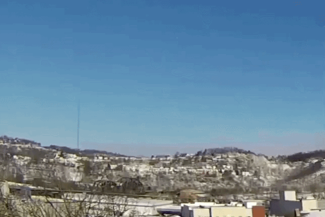 Clear blue sky over a desert town with light-colored, low-rise buildings spread across rolling hills; a tall antenna rises on the left.