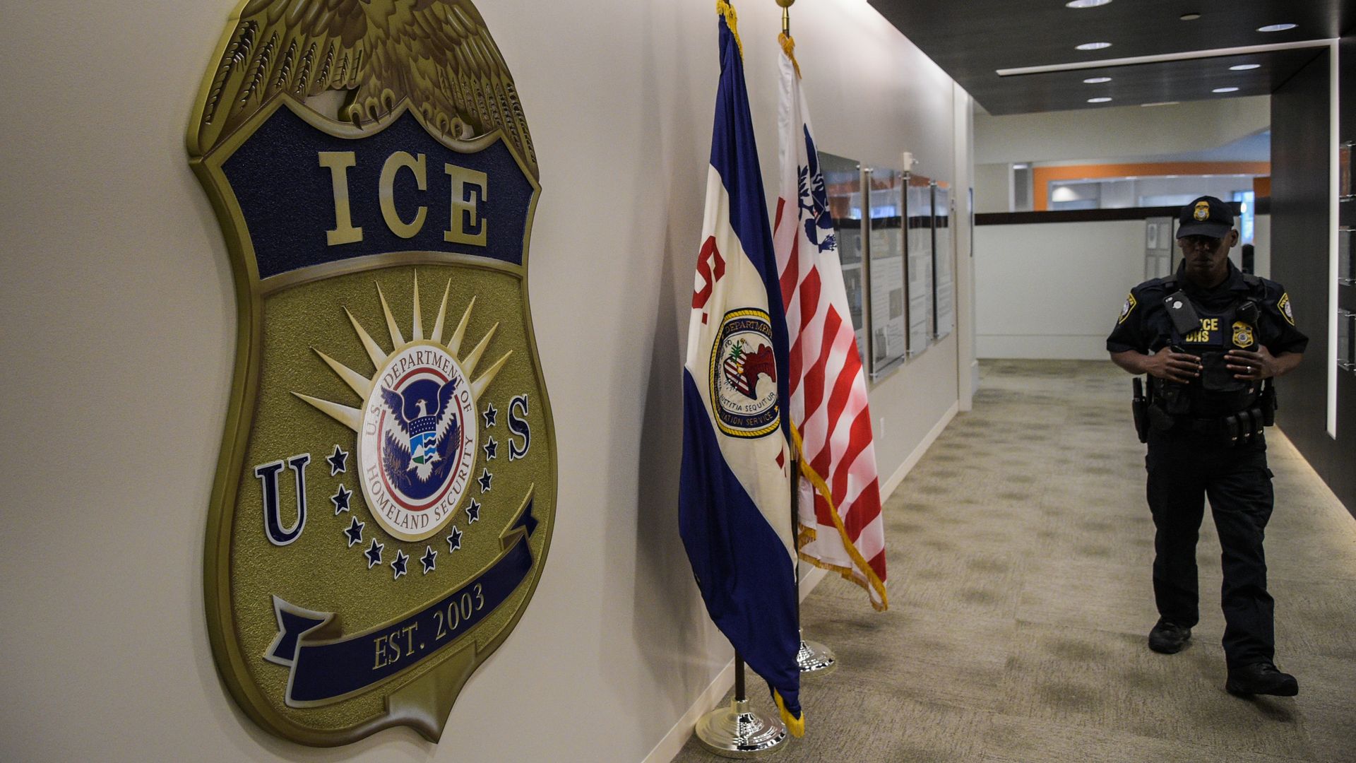 ICE sign on a wall with an officer walking down a hallway