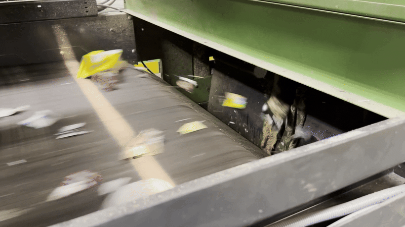 Animated gif shows a high-speed conveyor belt with a beam of light across it used to sort recyclables. 