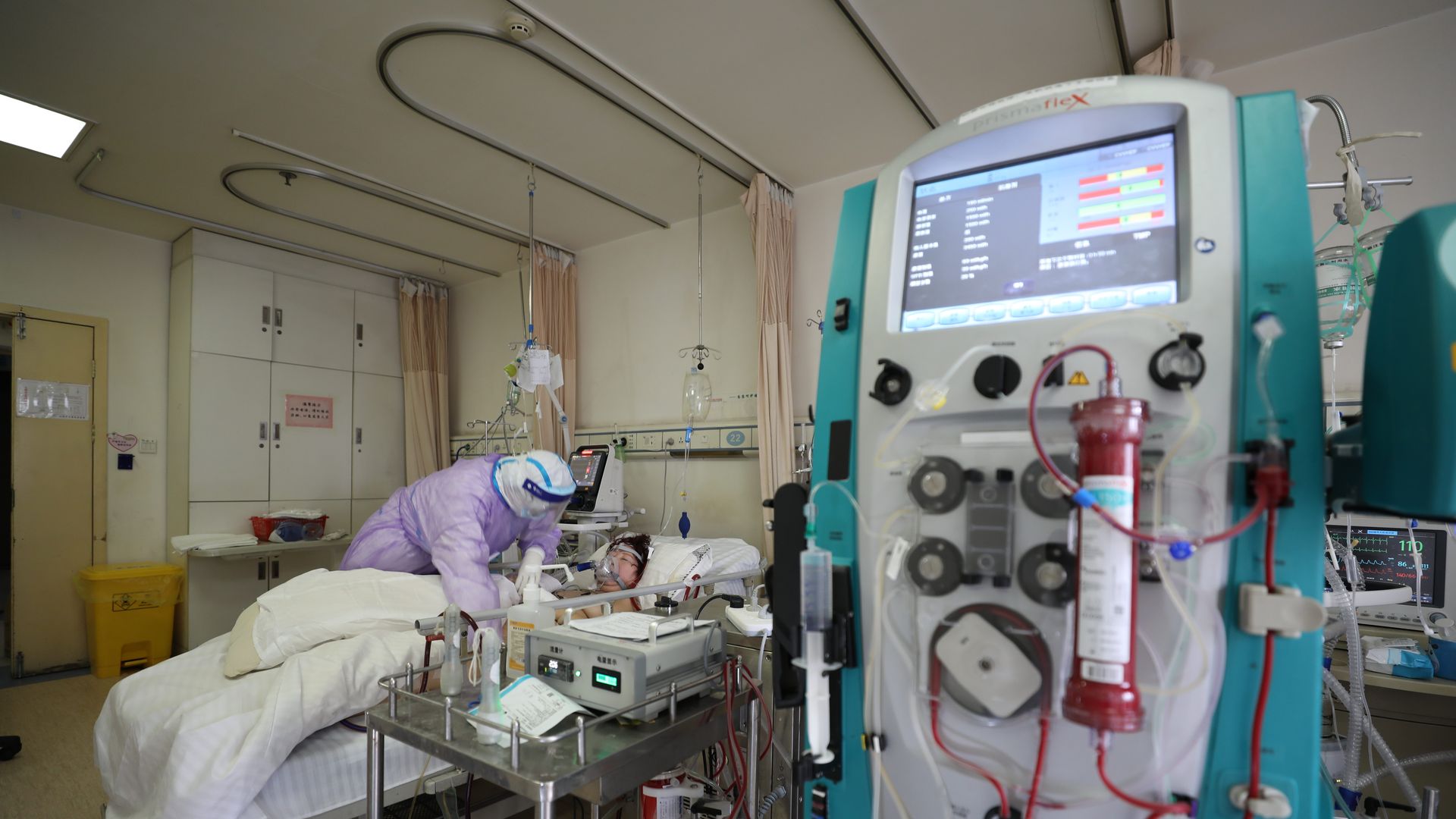 A nurse cares for a patient in a hospital intensive care unit with a blood machine in the foreground.
