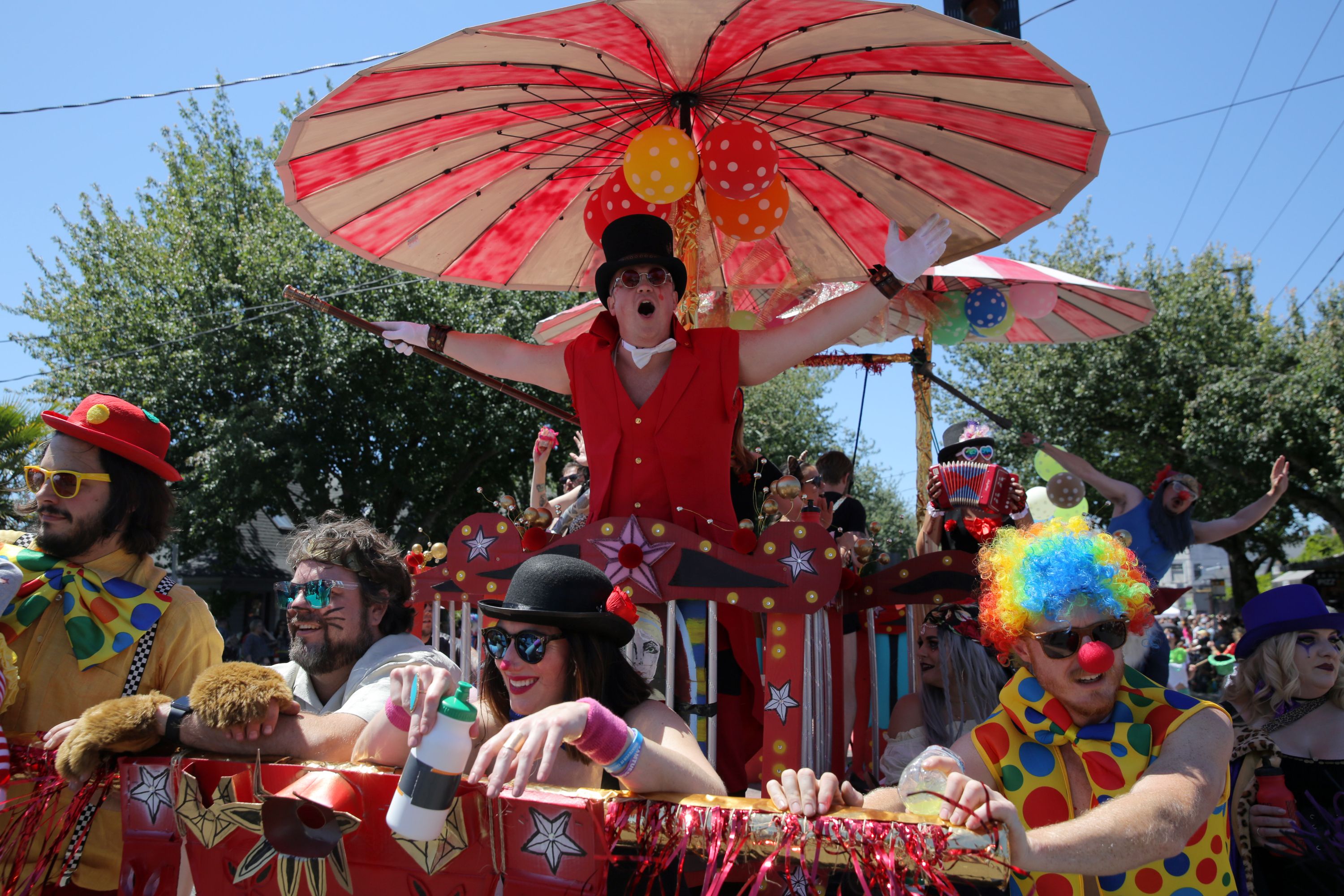 A red carnival float with a large striped umbrella over a man in a top hat and a clown.