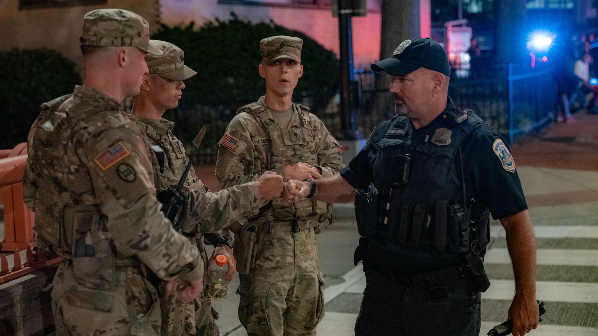 National Guard members fist bump a D.C. police officer on a city street at night