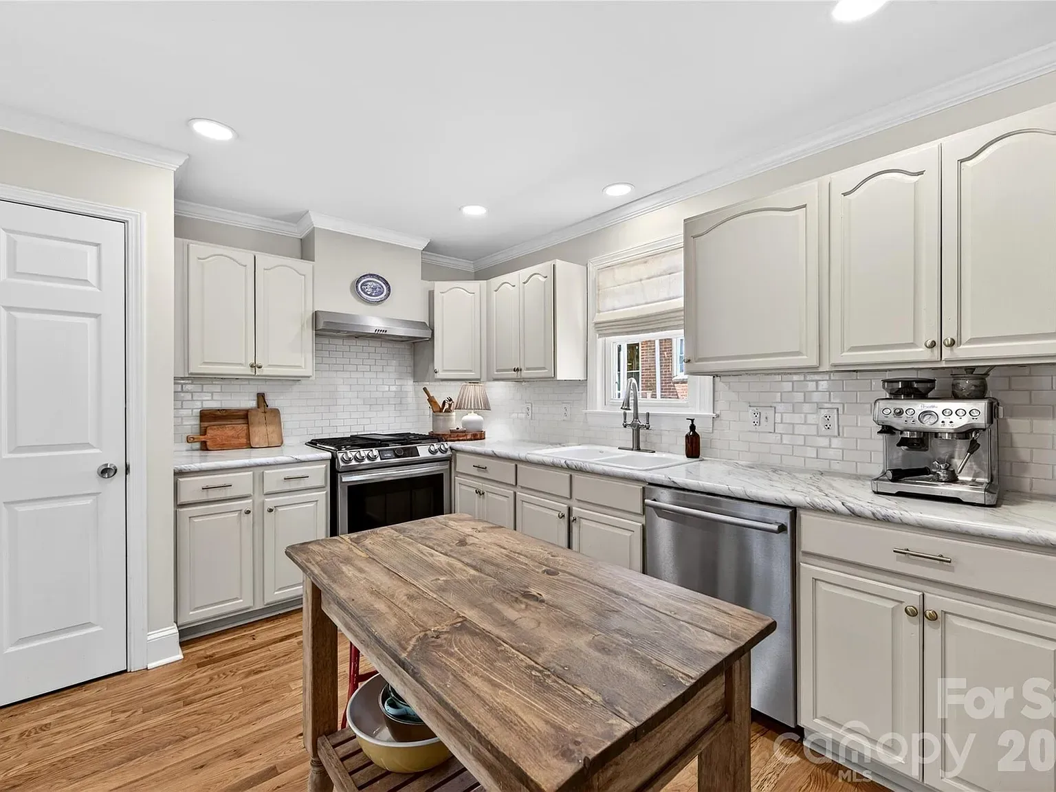 houses for sale charlotte. Bright, modern kitchen with white cabinets and marble countertops. Stainless steel stove and dishwasher, white subway tile backsplash, wooden island, and a window over the sink; coffee machine.