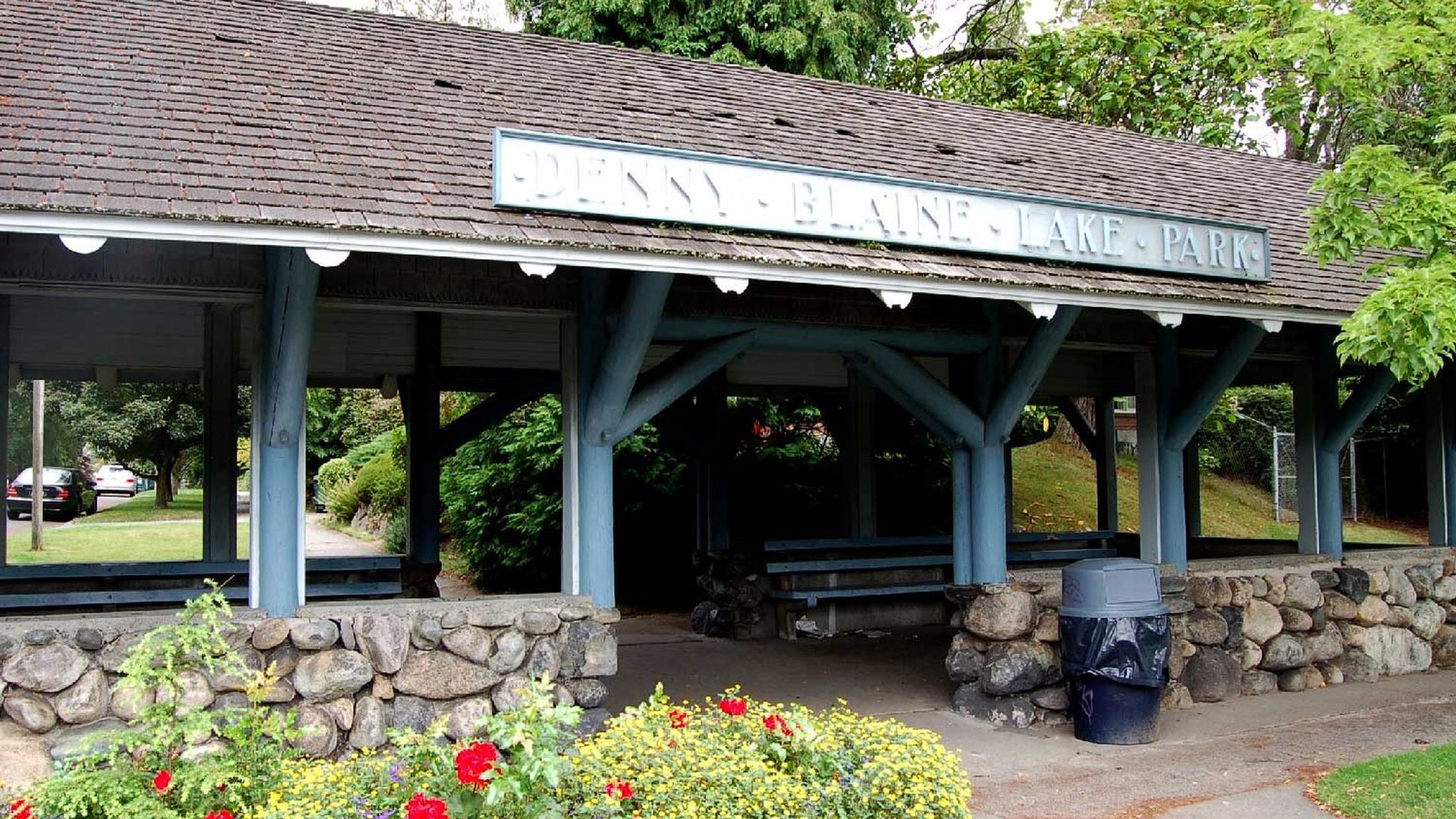 The covered entrance pavilion at Seattle's Denny Blaine Park, with the park's name displayed on the roofline above stone columns and flower beds in the foreground.