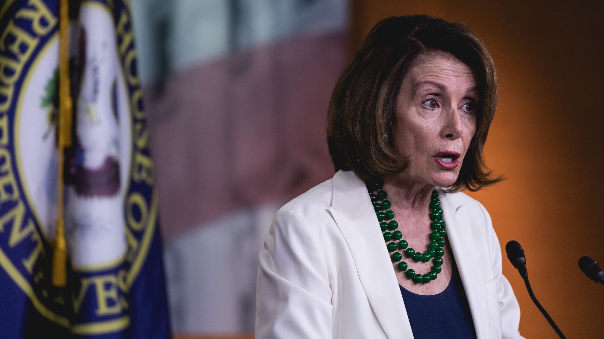 Nancy Pelosi standing at a podium speaking into a microphone