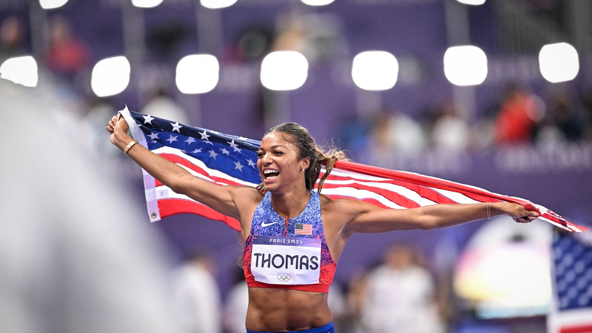 Gabby Thomas holding an American flag after winning a race.