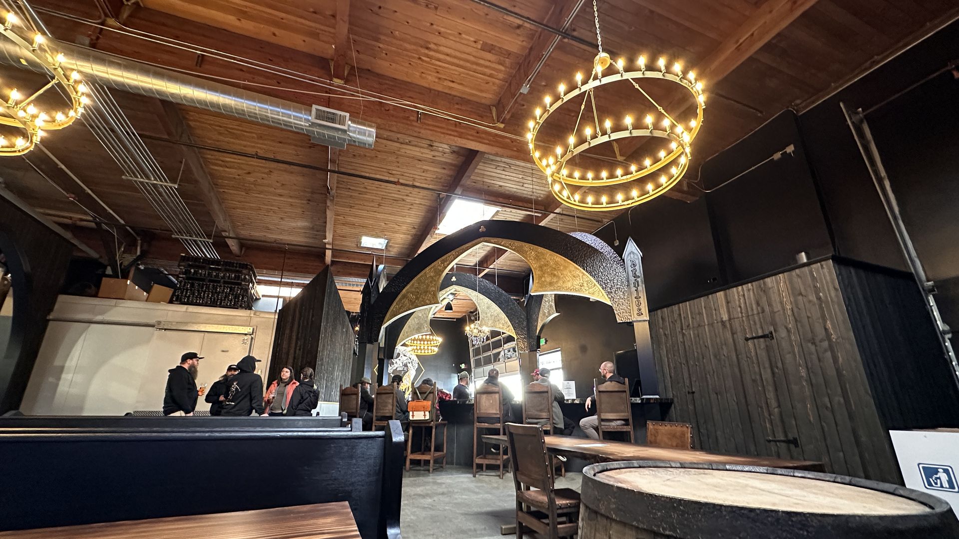 A brew pub interior with a round chandelier and five people sitting at the bar