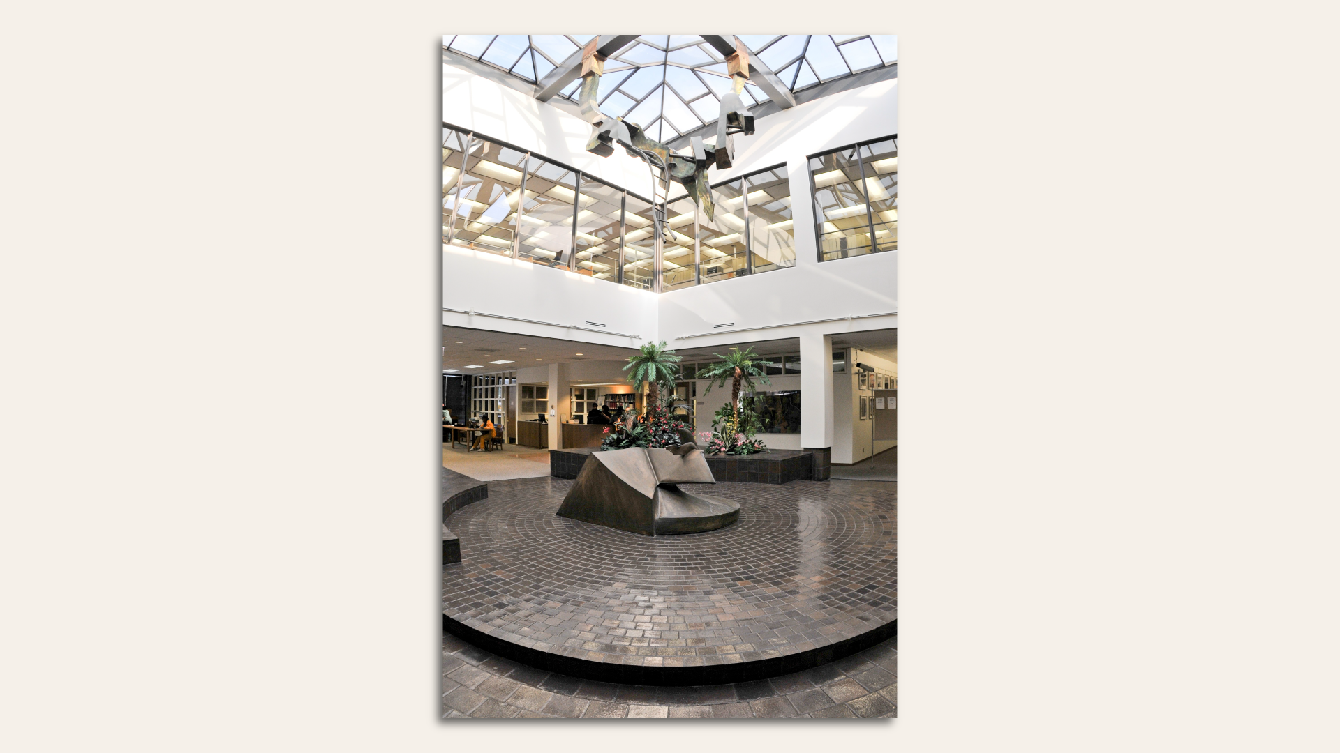 Glass atrium with bronze sculpture on a pedestal with one sculpture hanging from the ceiling.