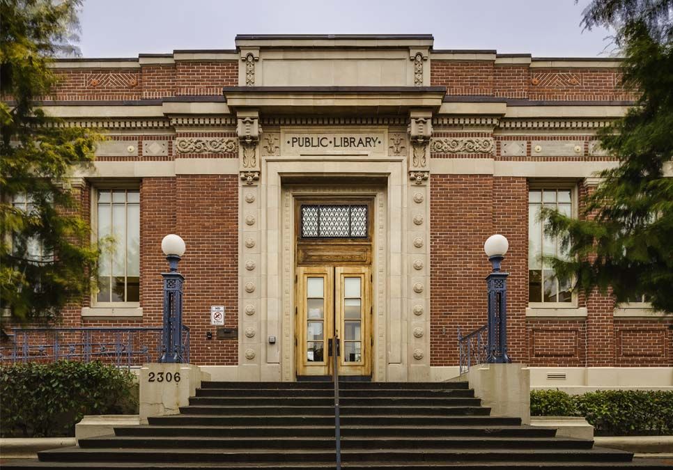 A brick building with steps up to doors with windows and decorative moldings, with two lamp posts on each side of the entrance.