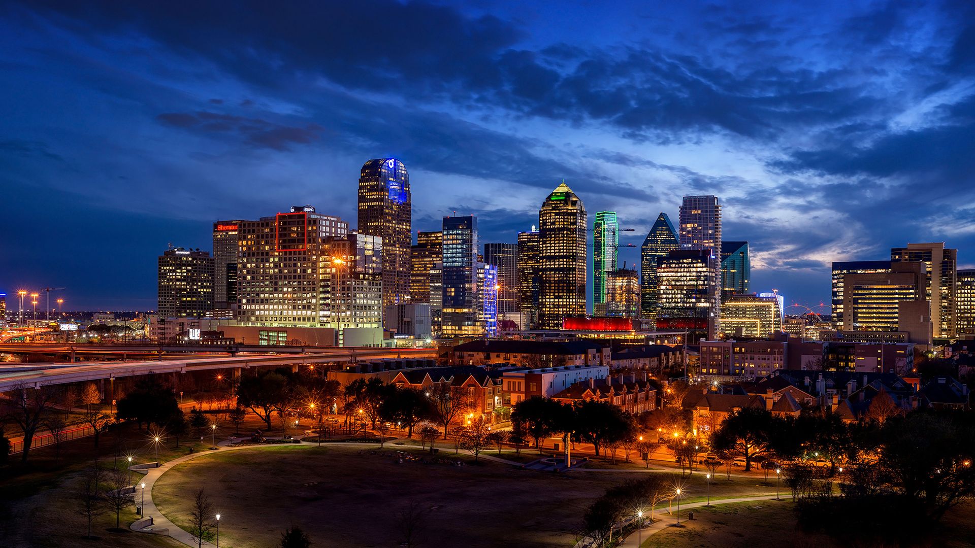 The Dallas skyline bright and glowing against a dramatic darkening sky.