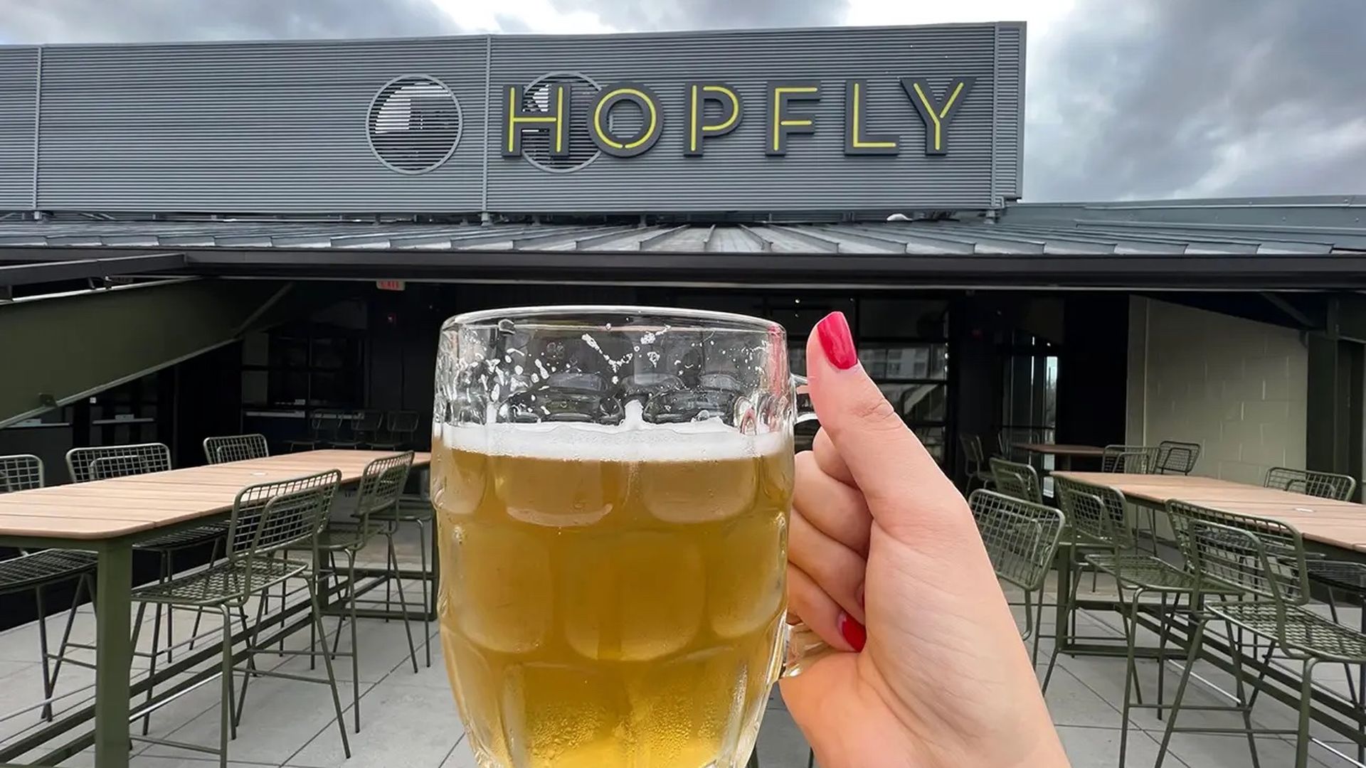 Hand holding beer mug on rooftop patio in front of sign that says "HOPFLY"
