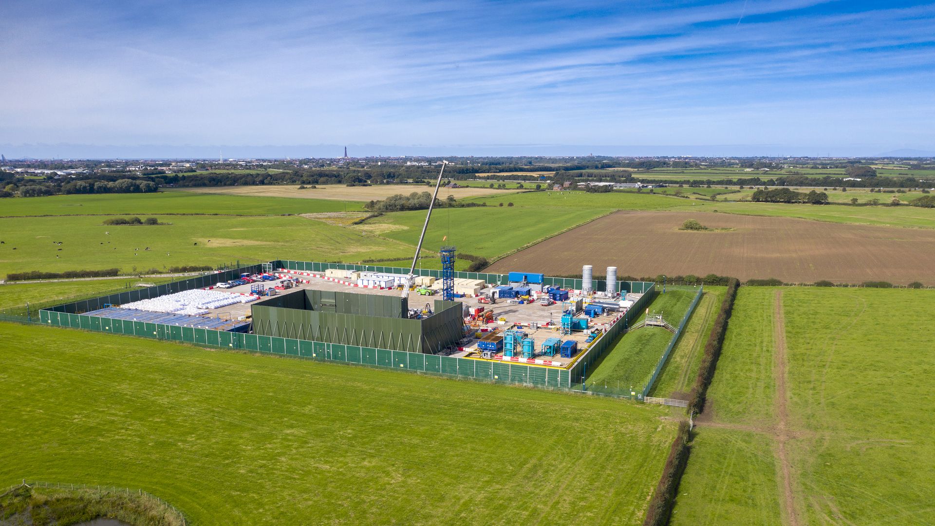 The photo shows a hydraulic fracking site in England, surrounded by verdant grass.