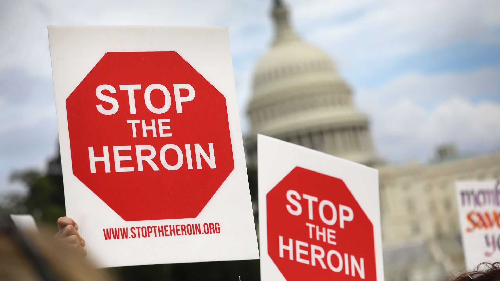 Protestors hold signs in front of the Capitol building that read "Stop the Heroin" 