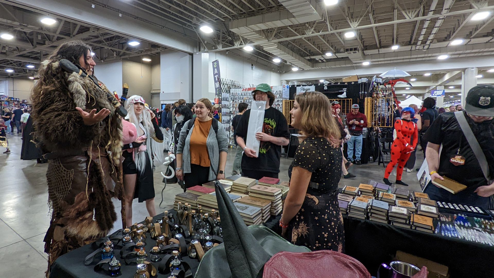 A man dressed as a wildling speaks with other visitors at a leatherworker's booth at a fan convention