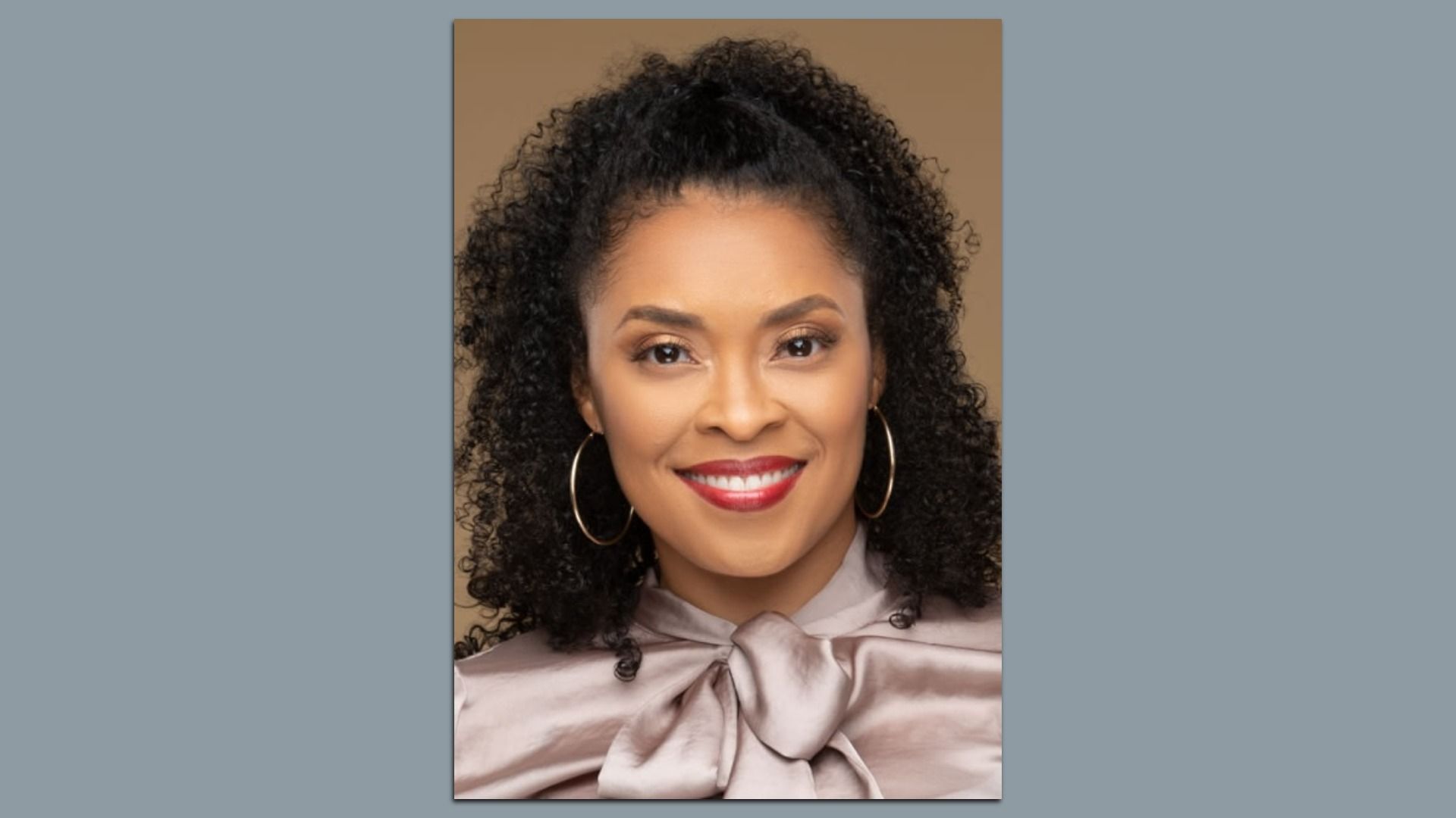 Headshot of woman with curly hair, hoop earrings and a silk blouse with a bow.