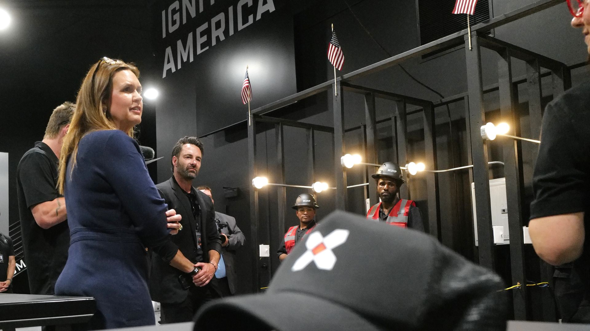 Arkansas Gov. Sarah Huckabee Sanders speaks to employees during a visit to a Unlock Human Potential facility, with workers and an "Ignite America" sign in the background.