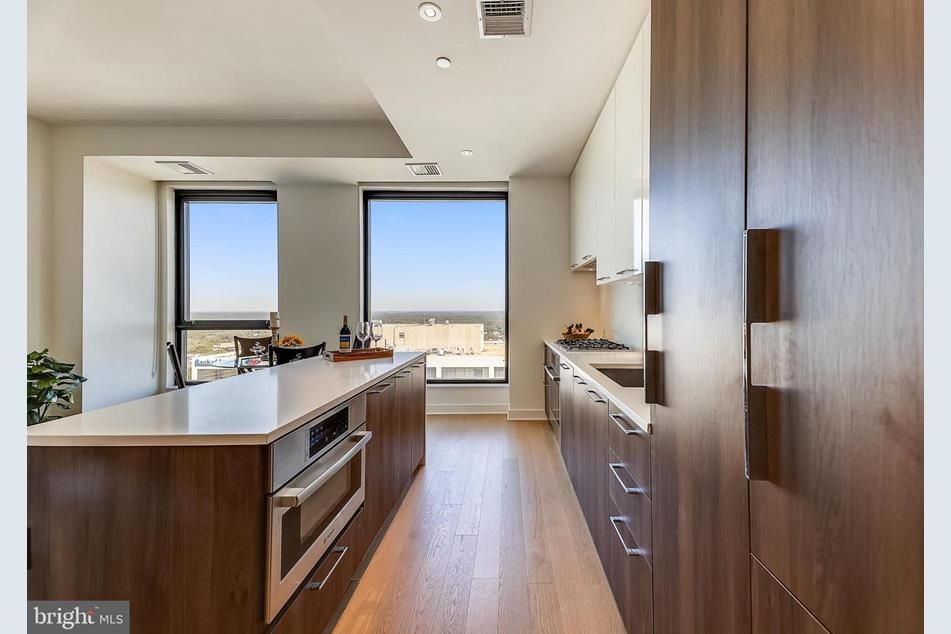 A condo kitchen/dining area with two large windows and wood cabinets. 