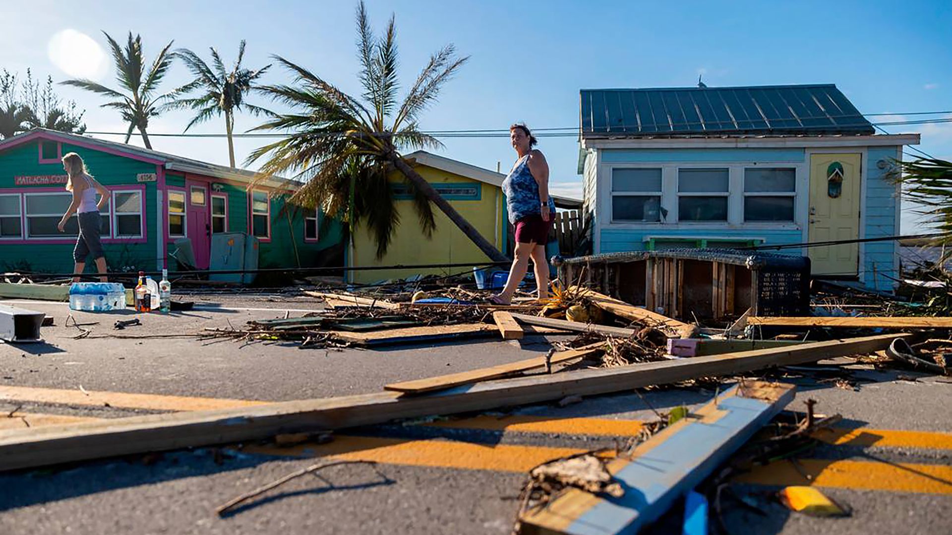 Women walk past wood and debris from a hurricane